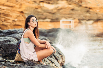 Pretty long hair brunette tourist girl relaxing on the stones near sea.