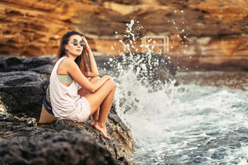 Pretty long hair brunette tourist girl relaxing on the stones near sea.