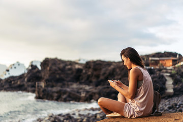 Pretty long hair brunette tourist girl relaxing on the stones near sea.