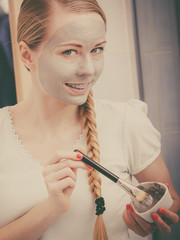 Happy young woman applying mud mask on face