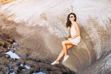Pretty long hair brunette tourist girl relaxing on the stones near sea.