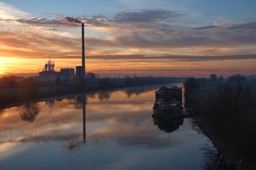 Scenic sunrise over the river with boat and chimney in the background
