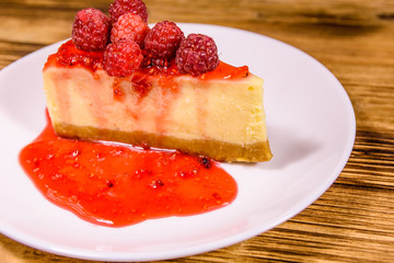 White plate with cheesecake New York and raspberries on wooden table