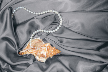 still life of large orange shells and white pearl beads on gray satin fabric, top view