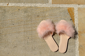 Elegant pink feather slippers on a stone floor on a sunny day