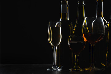 Bottles of wine and different glasses of wine on a dark background