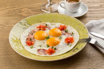 fried eggs with bacon and chopped tomatoes and cup of espresso on wooden table