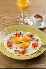 fried eggs with bacon and chopped tomatoes and cup of espresso on wooden table