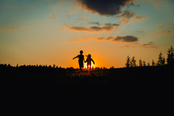Silhouette of happy boy and girl running play at sunset