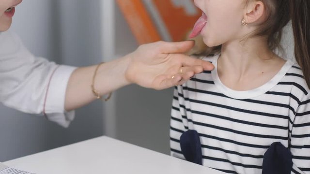 A woman physician examines a sore throat for a little girl patient. Mother and young daughter at a reception at the pediatrician, close-up.