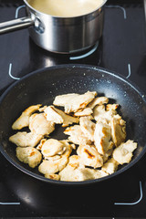 Food shot of cooking poultry meat slices on a black pan