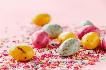 Fototapeta na wymiar Easter chocolate eggs candy with colorful sprinkles on a pastel pink background, creative easter concept, top view