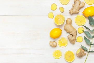 Whole and sliced fresh lemon, ginger root, eucalyptus leaves on white wooden background. Flat lay top view copy space. Minimal fruit concept design seasoning spice ingredient for tea. Yellow citrus
