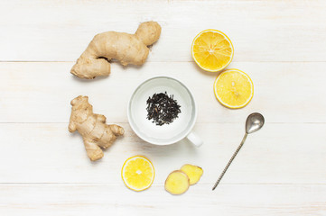 Fresh ginger root, cup tea with brewing inside, lemon on white wooden background. Flat lay, top...