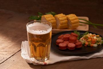 Grilled sausages with glass of beer on wooden table with copy space.