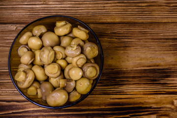 Glass bowl with canned mushrooms on wooden table. Top view