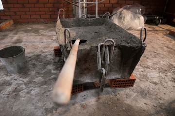 Worker shovels a wet mix of concrete from a wheelbarrow at curb block installation. Kerb edging at sidewalk construction.