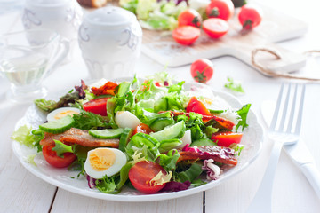 Fresh salad of roasted bacon, cherry tomatoes, quail eggs on a white plate, horizontal