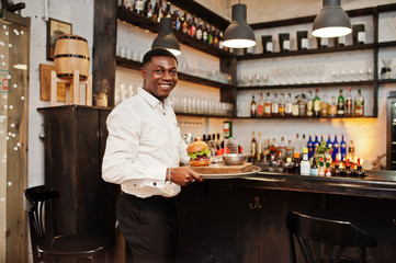 Young african american waiter man hold tray with burger at bar of restaurant.
