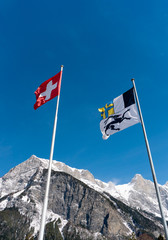 flags of Switzerland and the Grisons canton blowing in the wind in a blue sky in the mountains