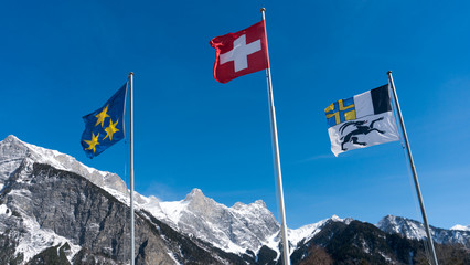 three flags waving in the wind in a mountain landscape in the Swiss Alps