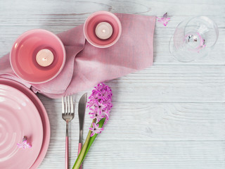 Pink rustic place setting with purple hyacinth flower, candles and linen napkin on white wooden background