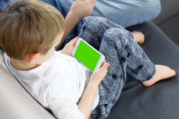 Boy sitting and using mobile smart phone with green screen at home. Close up of thumb scrolling up through touch screen display