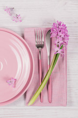 Pink rustic table setting with purple hyacinth flower and linen napkin on white wooden table
