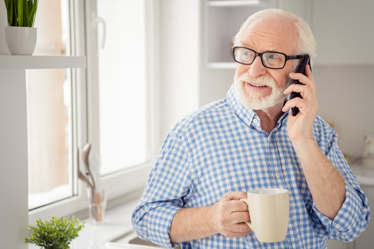 Close up portrait grey haired he his him grandpa hot beverage hand arm tell children health condition telephone smart phone user wear specs casual checkered plaid shirt jeans denim outfit room kitchen