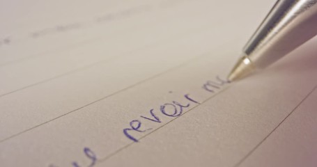 Sliding macro shot of a pen tip writing French words on paper