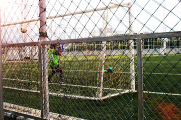 Fototapeta premium Blurred of men practice football give Boys with green grass yard have Metal wire Block area In the evening sun Shine.