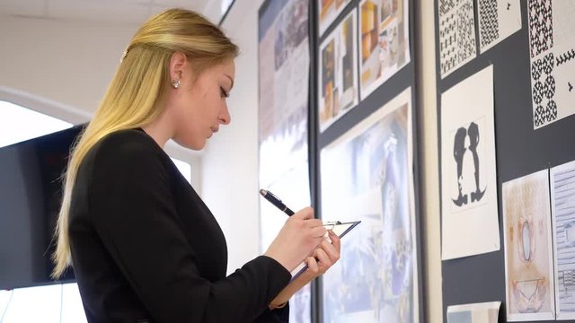 Young female designer looking checking mood board and making notes. Beautiful attractive woman, designer, looking on the creative board with arts and making notes.