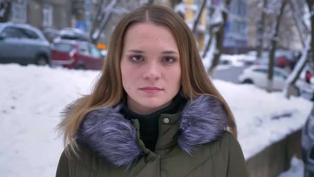 Closeup shoot of young attractive caucasian brunette female standing outdoors in a winter coat in a snowy day