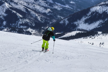 Boy is turning on other side for next arc on skies. A male skier skiing freeride in Slovakia mountains, Low Tatras. Yellow helmet. Ski poles