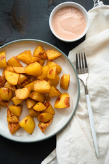 Plate of hot Patatas Bravas, a traditional Spanish tapas dish, oven baked potato cubes until crispy served with spicy aioli garlic sauce seasoned with chili and paprika on dark wooden background