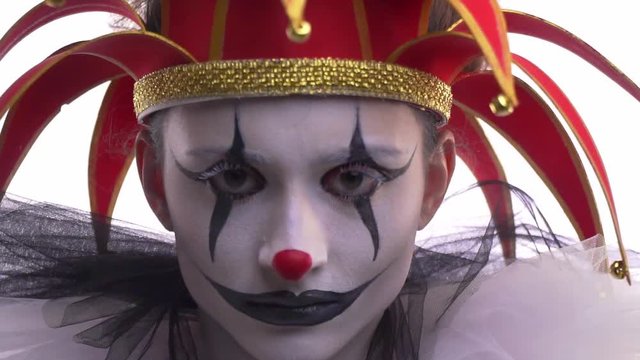 A female jester is wearing a red hat and black and white makeup, close up