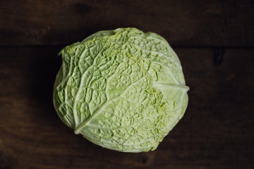 Close up of head of fresh, green savoy cabbage with its crinkled leaves, a healthy winter vegetable, ready for cooking preparations on dark wooden kitchen table