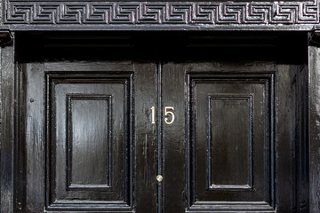 House number 15 in bronze on a black wooden entrance door with the fifteen in bronze and intricate...