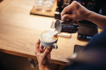 Barista hand pours cream into the cup of coffee