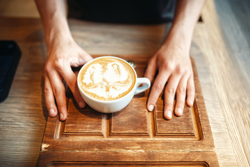 Barista holds cup of coffee with foam drawing