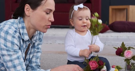 Mother and her cute baby girl playing with rose flowers at home