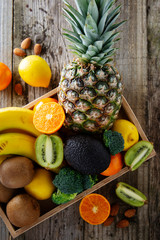 Fruits on wooden background - pineaple, tangerine, orange, citrus fruits, kiwi, broccoli. Healthy food, lose weigh. Copy space. Fruits and vegetables. Avocado.