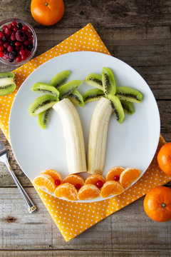 Naklejki Fun and healthy fruit salad for kids, kiwi banana mandarin palm trees. Healthy food for children.