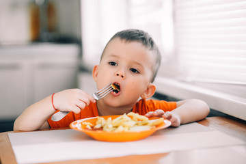 beautiful baby in orange t-shirt with orange plate eating fried French fries