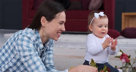 Happy mother with cute baby daughter arranging rose flowers at home