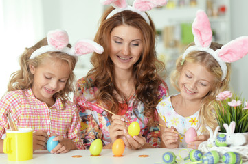 Mother with her cute daughters wearing rabbit ears and painting Easter eggs