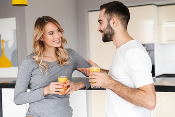 Young loving couple at the kitchen drinking juice talking with each other.