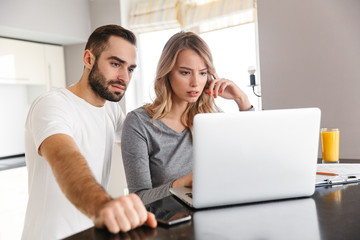 Young loving couple sitting at the kitchen using laptop computer.