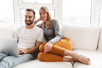 Amazing loving couple sitting indoors at home using laptop computer.