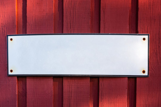 A white blank empty steel sign with copyspace on a red wooden barn wall.